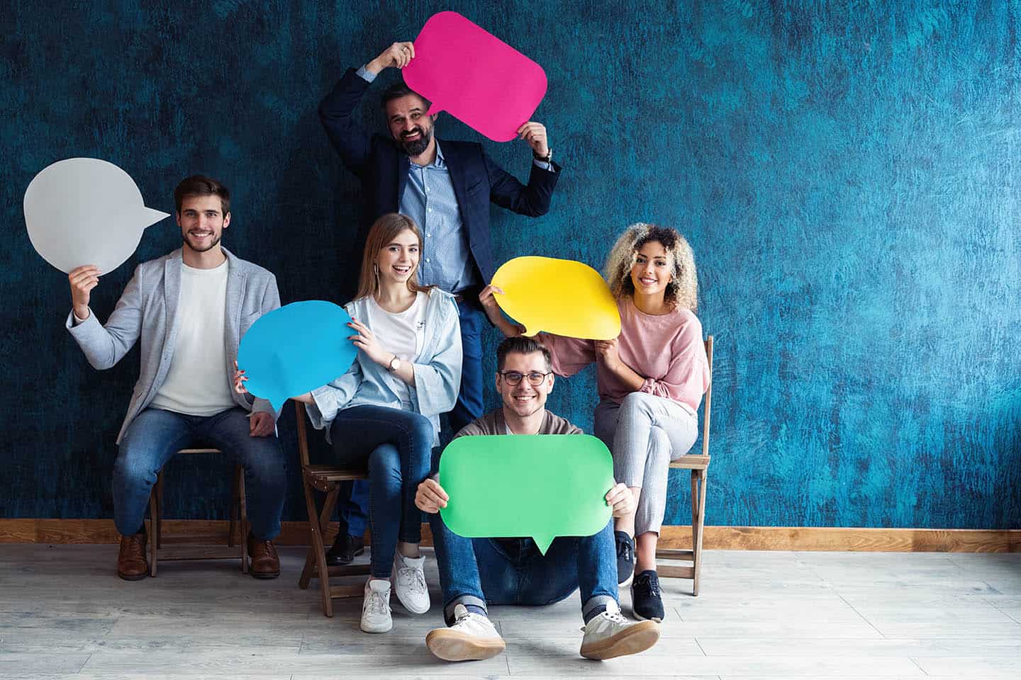 Let's start a conversation. We speak the language of success. Diverse group of businesspeople holding up speech bubbles while they wait in line
