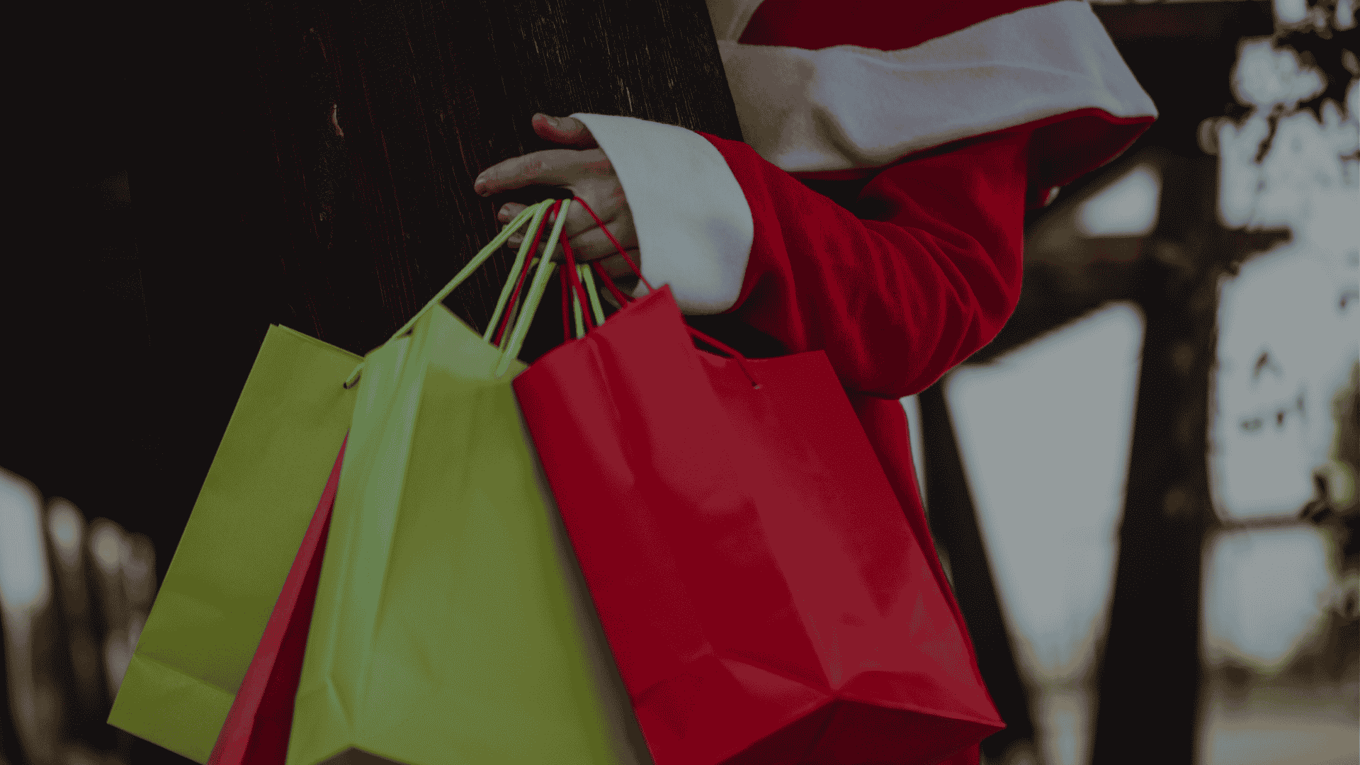Person wearing a red-and-white outfit holding multiple colorful shopping bags outdoors.