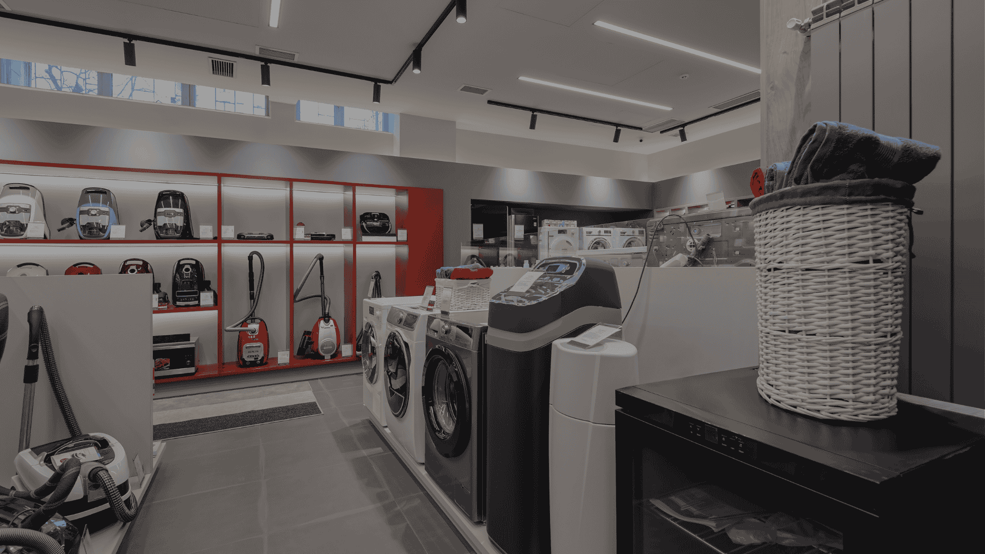Interior of an appliance store displaying washing machines, vacuum cleaners, and other electronics.