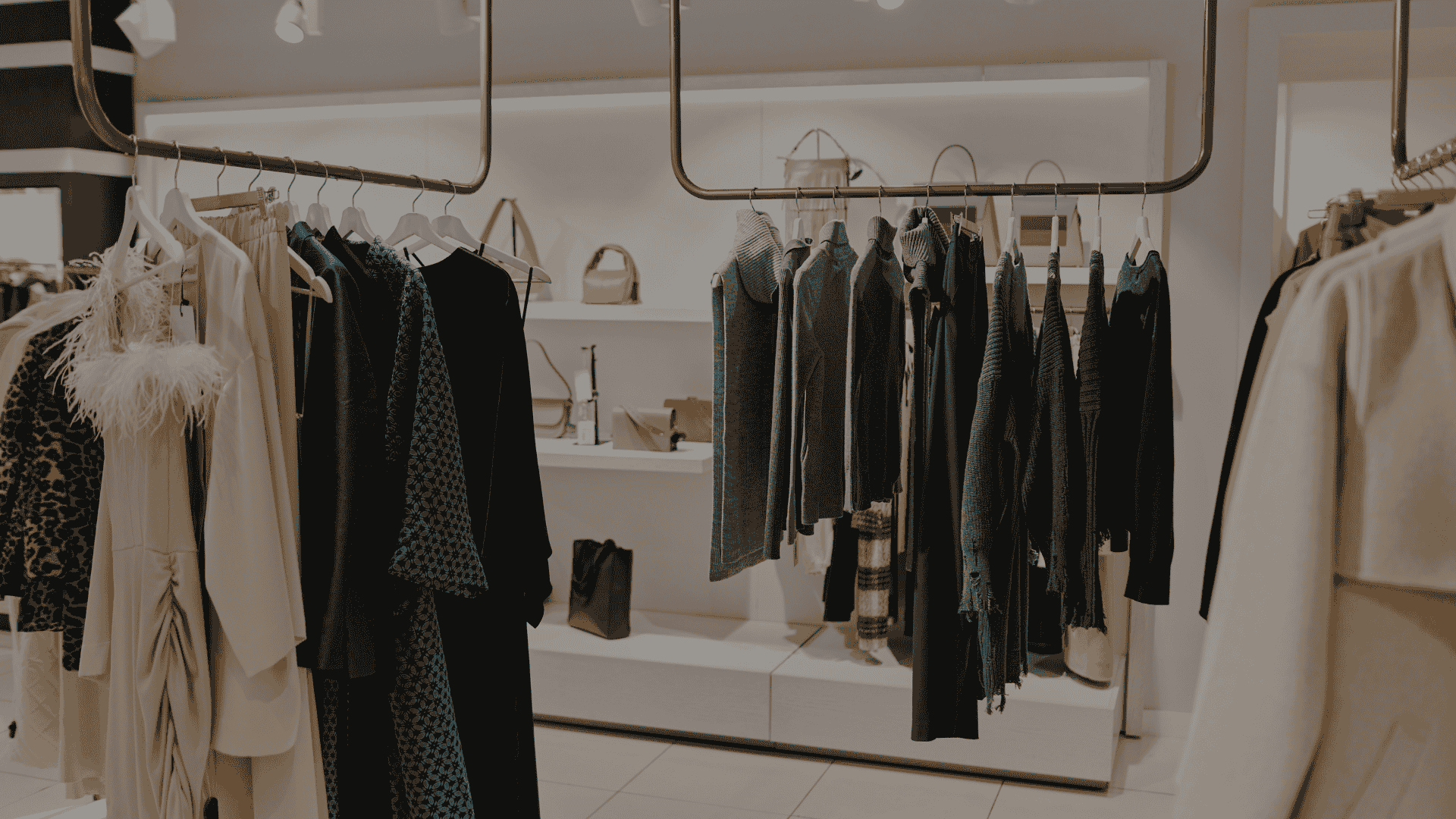 Boutique store featuring a variety of clothing items hanging on gold racks, with shelves displaying bags and accessories.