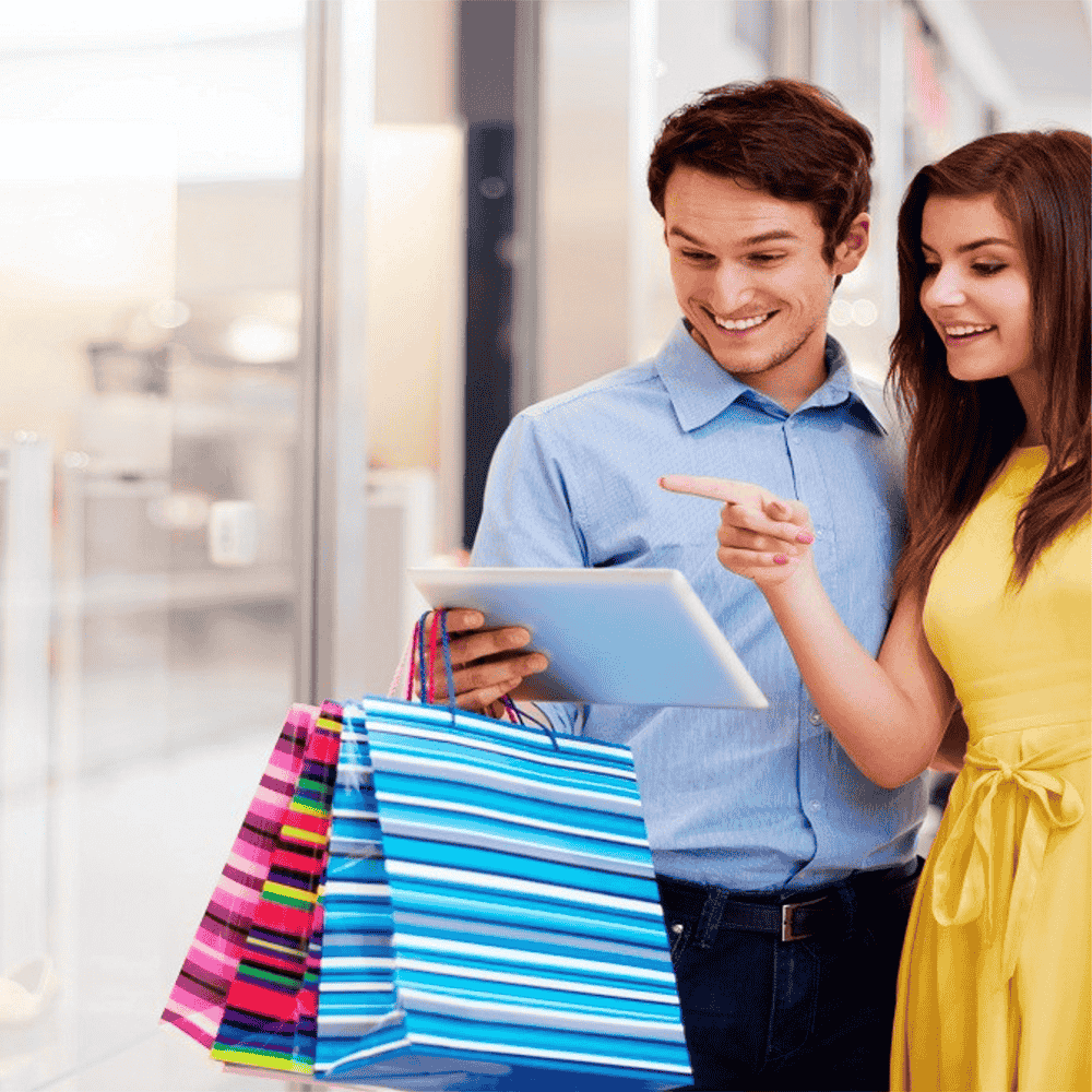 a man and a woman carrying shopping bags looking at something excitedly