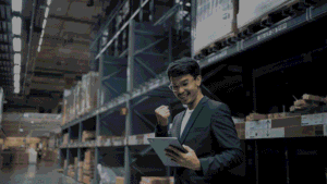 A warehouse manager in a blue blazer smiling and celebrating while reviewing data
