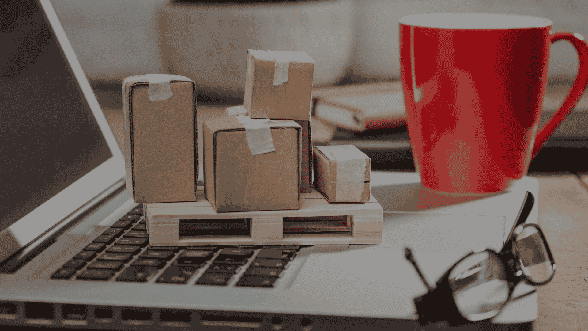 Miniature shipping boxes placed on a laptop symbolize how an Order Management System order processing across multiple sales channels.