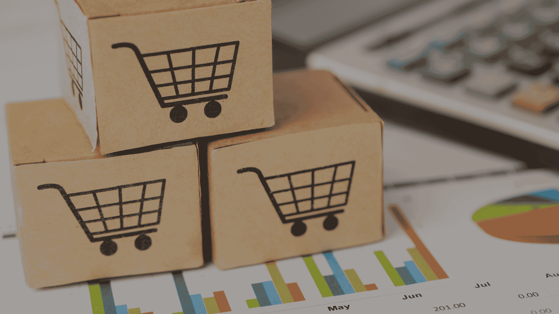 Three cardboard boxes with shopping cart symbols stacked on top of retail sales charts and business analytics reports.