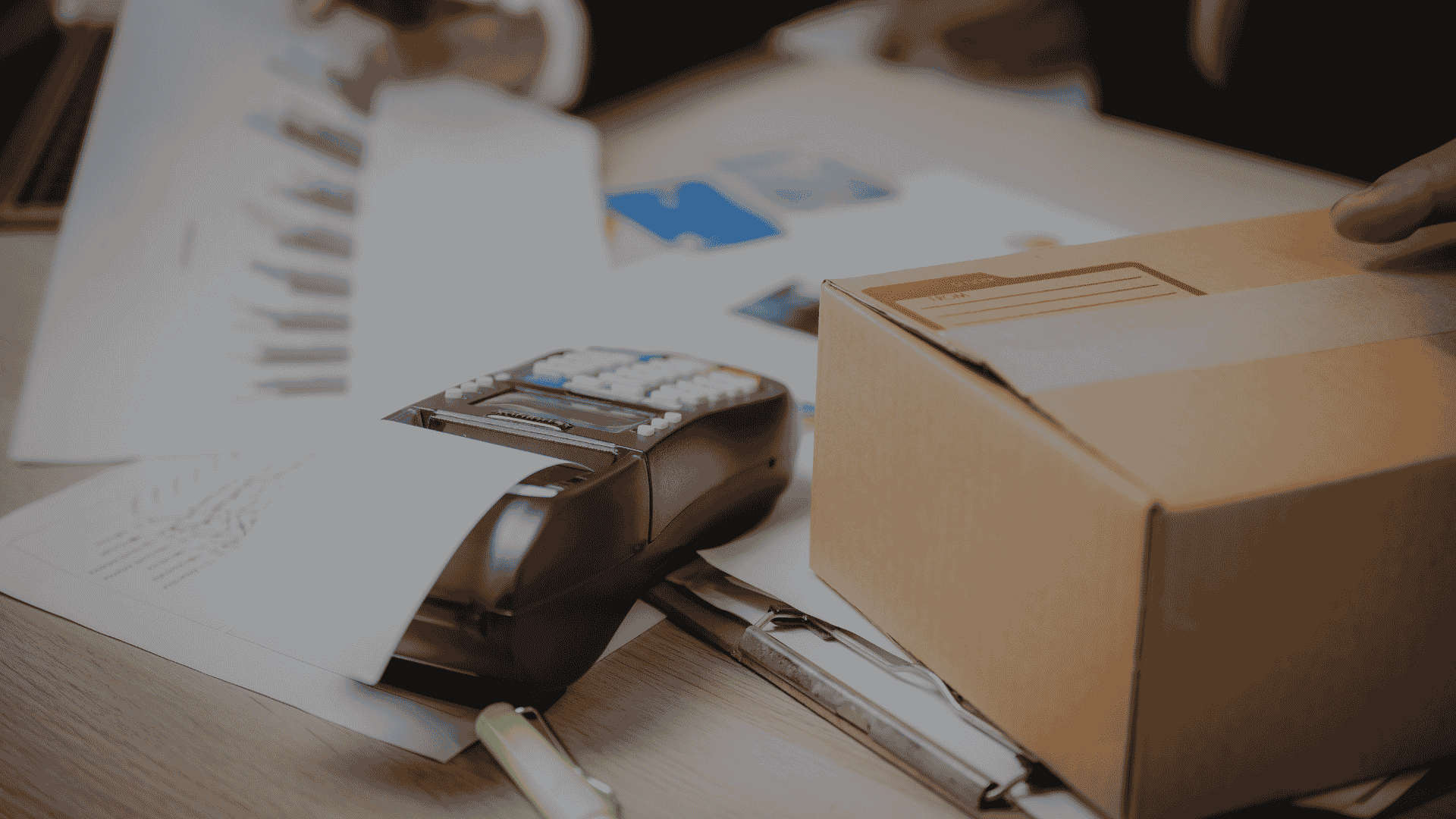 Close-up of a card payment terminal printing a receipt on a desk, next to a taped cardboard parcel