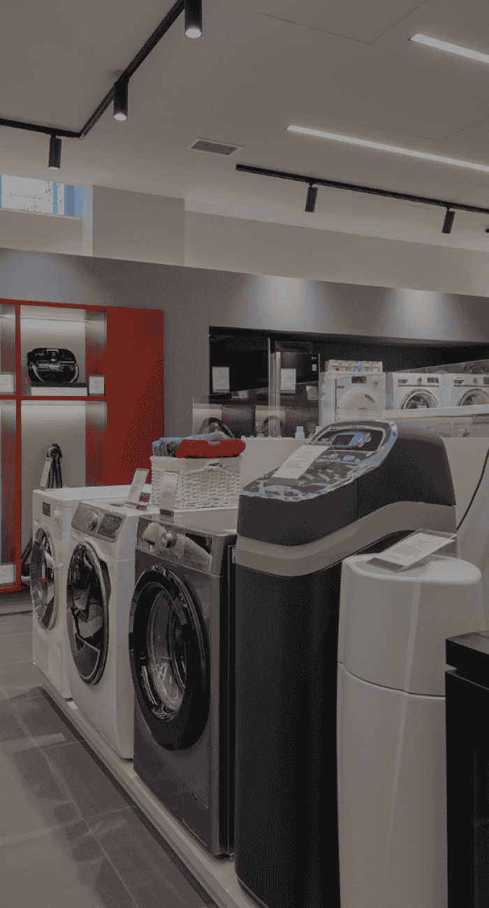 Interior of an appliance store displaying washing machines, vacuum cleaners, and other electronics.